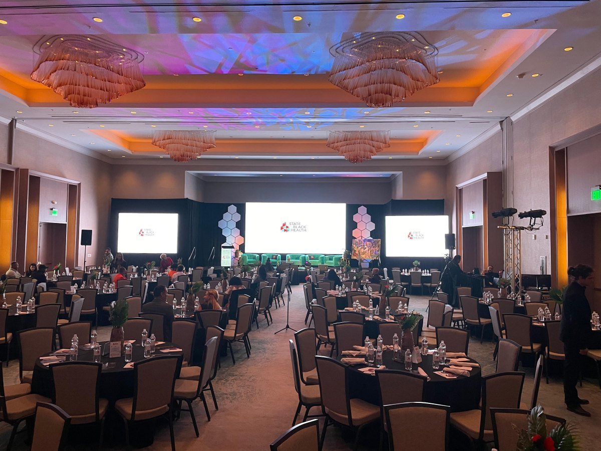 Ballroom set for a banquet with three projection screens, a lounge-style stage and colorful gobo patterns on the ceiling