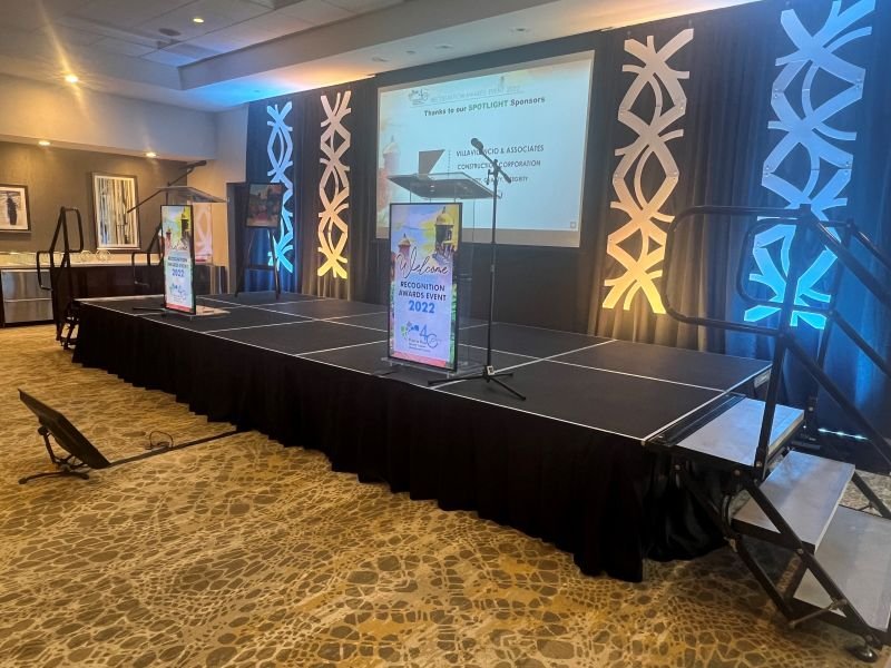 Event stage with black skirting, a clear podium and backlit scenic panels in blue and amber light